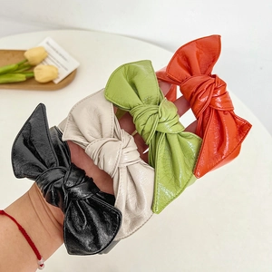 Detail view of four vintage faux leather bow headbands in black, white, green, and orange