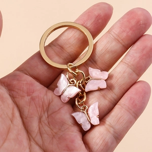 Detail of hand holding a golden keychain with three light pink sequin butterfly charms