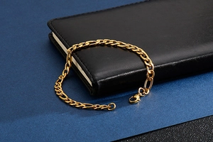 Macro shot of golden Figaro chain bracelet with lobster clasp on leather notebook