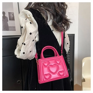 Détail d'un sac bandoulière rose rouge avec motif cœur gaufré et une bandoulière amovible