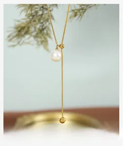 Detail einer verstellbaren goldenen Y-Kette mit weißer Perle und Schlangenkettentextur