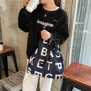 Detail of dark blue canvas tote bag with letter print paired with a black sweater