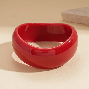 Detail of a wide red acrylic resin bangle on a beige textured background with a decorative stone