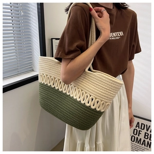 Detail view of woven straw tote bag in cream and olive green being worn by a model