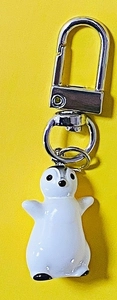 Detail of cute 3D resin penguin keychain with silver metal D-ring clasp on yellow background