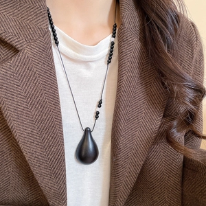 Detail of waterdrop wood pendant necklace with black beads worn by a female model