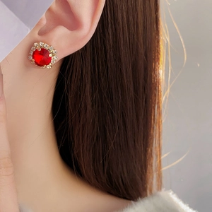 Close-up of elegant gold stud earring with a red round stone and halo crystals on a model