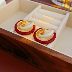 Détail de boucles d'oreilles en émail rouge et blanc sur velours dans une boîte en bois