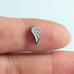 Delicate silver angel wing charm made of stainless steel displayed on a fingertip