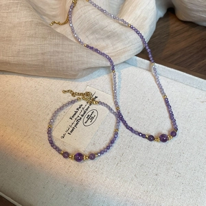 Detailed view of amethyst beaded necklace and bracelet set with golden accents on linen