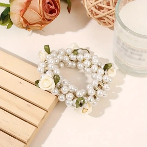 Close-up of white faux pearl hair tie with cream fabric roses and green ribbon leaves
