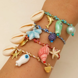 Detail of bohemian woven shell bracelets with sea star and dolphin charms on wrist