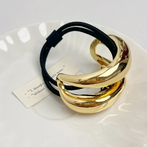 Detail of minimalist gold double-layer curved metal hair tie on a white ceramic tray