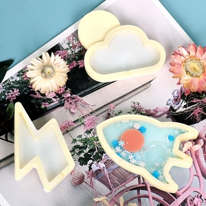 Detalle de moldes de silicona con forma de nube y cohete con resina azul y purpurina