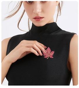 Detailed close-up of a luxury maple leaf brooch with pink rhinestones on a black knit top