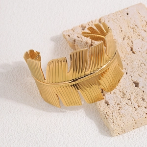 Detail of golden stainless steel cuff bracelet with textured tropical palm leaf design
