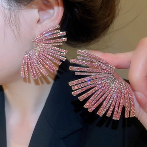 Macro shot of fan-shaped gold earrings with pink rhinestones on black clothes
