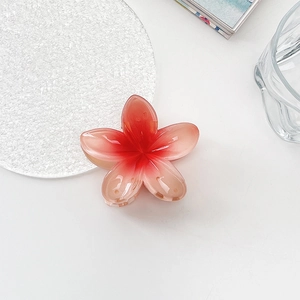 Close-up of a pink gradient plumeria flower hair claw clip on a white decorative table