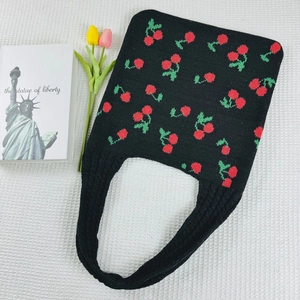 Detailed view of black knitted tote bag featuring red cherry patterns and woven handles