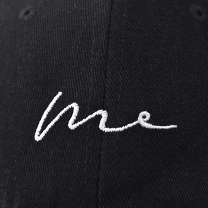 Macro shot of white 'me' embroidery on black cotton twill fabric of the baseball cap