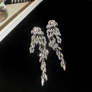 Close-up of silver tassel earrings with leaf patterns and shimmering crystal accents
