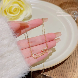 Close-up of gold Queen letter pendant with zircon crown held by hand over roses
