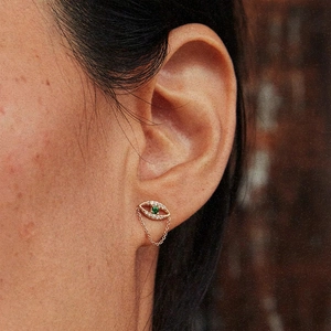 Macro shot of silver evil eye stud earring with green gemstone and dangling gold chain