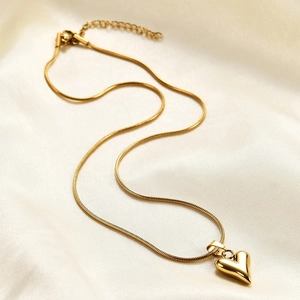 Detailed view of a gold heart pendant necklace with elegant snake chain on white silk