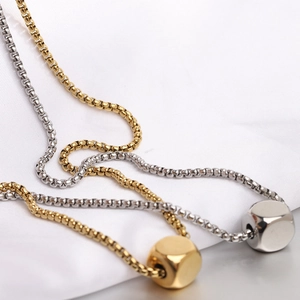 Close-up of minimalist gold and silver cube necklaces on white silk and reflective surface