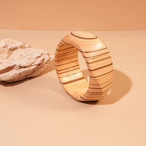 Macro view of wide wooden bangle showing natural stripes and wood grain on beige surface