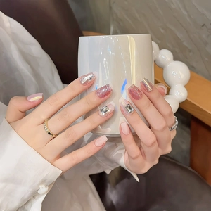 Handmade press-on nails with aurora pink glitter and large rhinestones on a coffee cup