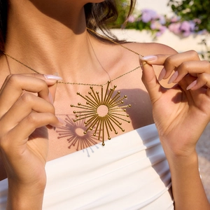 18K gold plated stainless steel sunburst pendant necklace worn by a model in natural light