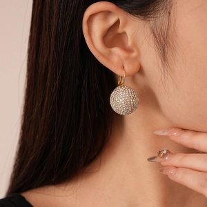Gros plan d'un modèle portant une boucle d'oreille dorée avec boule pavée