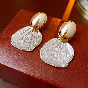 Detailed close-up of gold stud and silver shell earrings on brown leather gift box