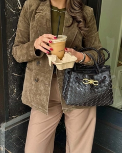 Dettaglio di una borsa in pelle intrecciata nera con nodo metallico e texture urbana