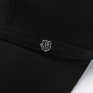 Dettaglio ravvicinato di un cappello nero con trama diagonale ed emblema a scudo in metallo