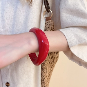 Close-up of a chunky vibrant red acrylic bangle featuring a smooth and rounded retro design