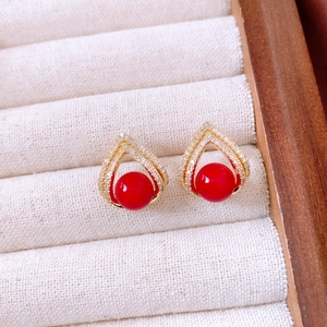 Détail de boucles d'oreilles perles rouges dorées et strass sur boîte à bijoux beige