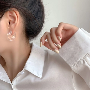 Close-up of transparent jelly-colored C-shaped hoop earrings worn by a female model