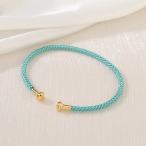 Detailed close-up of light blue braided rope bracelet with golden spherical metal end caps