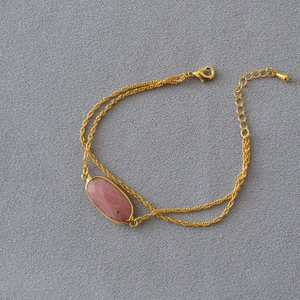Dettaglio del bracciale a doppia catena dorata con pietra rosa ovale e chiusura a moschettone