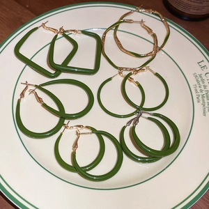 Flat lay of multiple green drip oil earrings in geometric shapes on a white plate