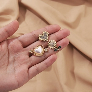 Goldenes Brosche-Set mit Strass-Herz und Sonnenblume vor beigem Stoffhintergrund