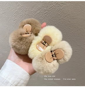 Hand holding three plush faux fur hair claws in brown, khaki and cream colors