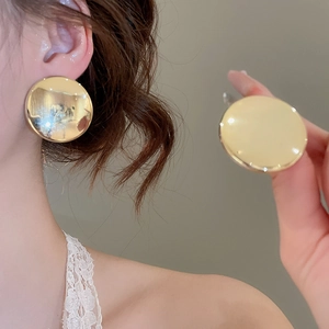 Gros plan de grandes boucles d'oreilles nœud en métal doré poli portées par un modèle
