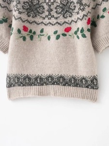 Detailed embroidery of red flowers and green leaves on a beige knitted sweater