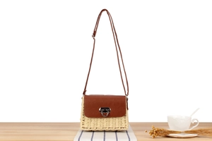 Detail of woven straw shoulder bag with dark brown faux leather flap and metal D-buckle