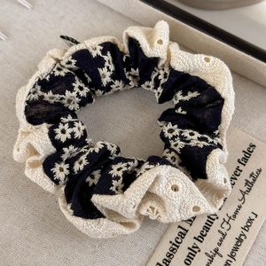 Detail of navy blue linen scrunchie with daisy embroidery and beige lace trim edge