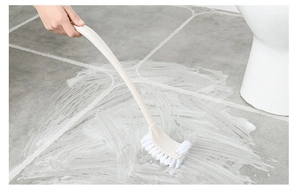 Detail of long-handle beige toilet brush cleaning foam on grey tile bathroom floor