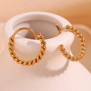 Detailed shot of gold-plated twisted hoop earrings hanging on a white ceramic vessel